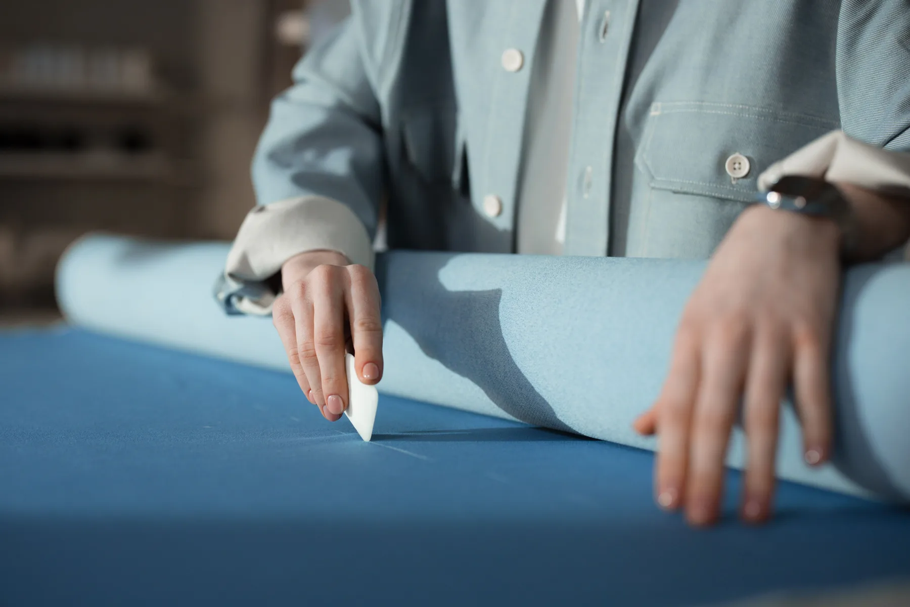 Tailoring hands marking blue cloth during garment construction.